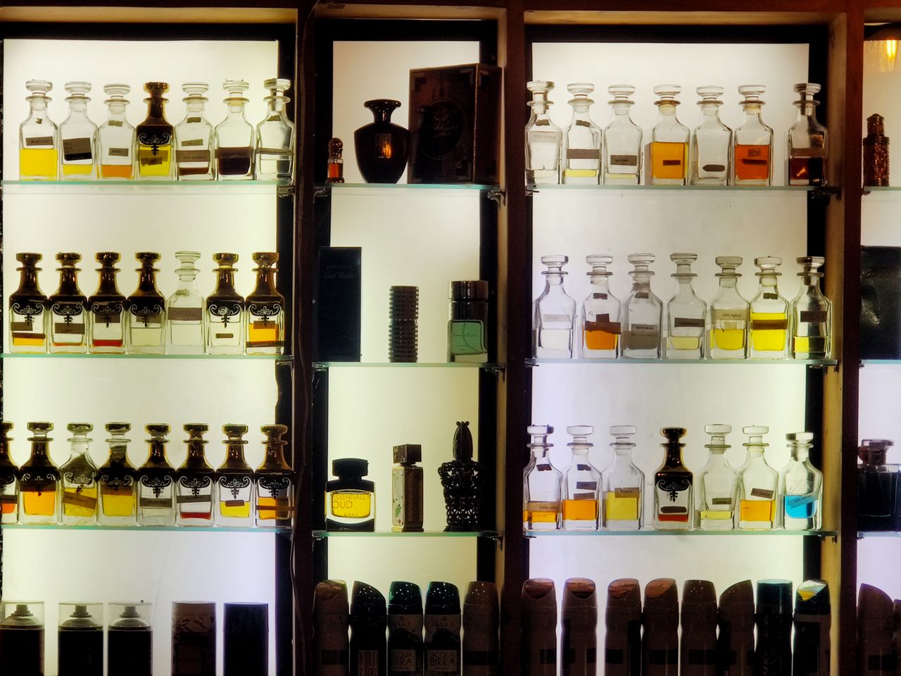 product-04 Aesthetic arrangement of diverse perfume bottles on illuminated shelves showcasing luxury fragrances.